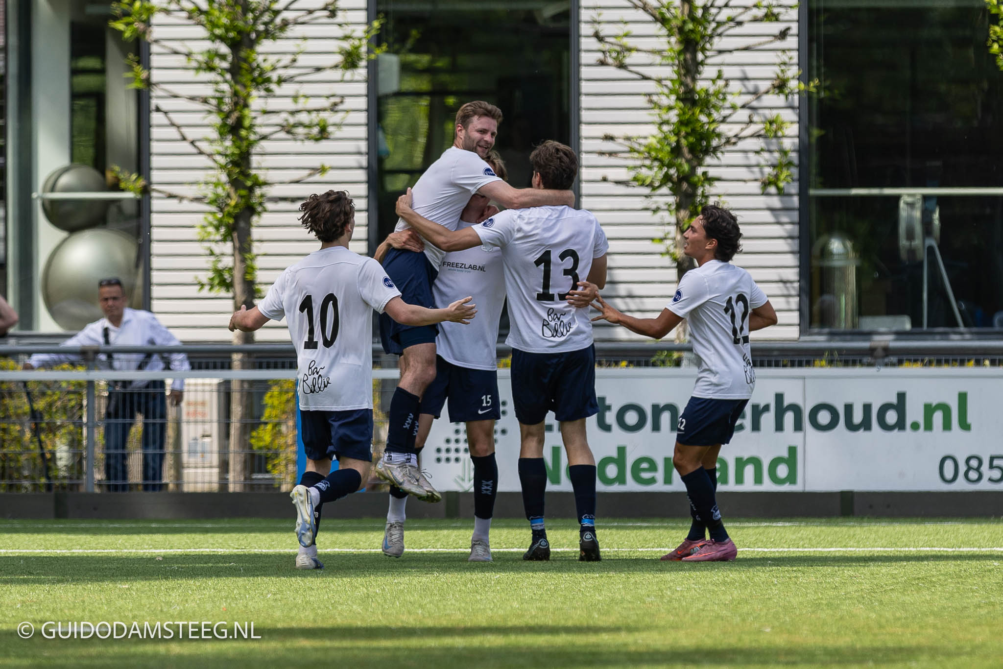 AVV-Swift-SDC-Putten-5-0-0N7A9877-20260530 - Guido Damsteeg - Guido Damsteeg Soccer players in white jerseys celebrate a goal, hugging near the sideline on a green field.